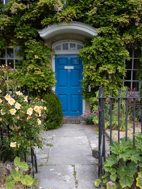A small front garden area featuring a decorative wrought iron table with an intricate circular pattern, flanked by two matching wrought iron chairs with ornate backrests and curved legs. The garden is
